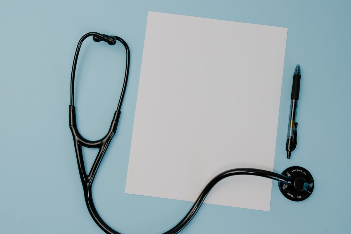 A stethoscope, blank paper, and pen on a blue surface; illustrative stock photograph.