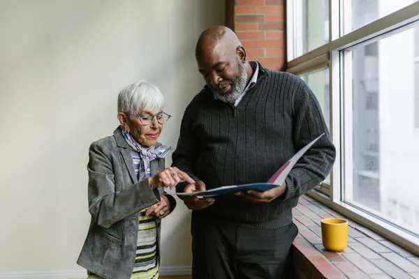 Two adults reviewing an open folder beside a window; illustrative stock photograph.