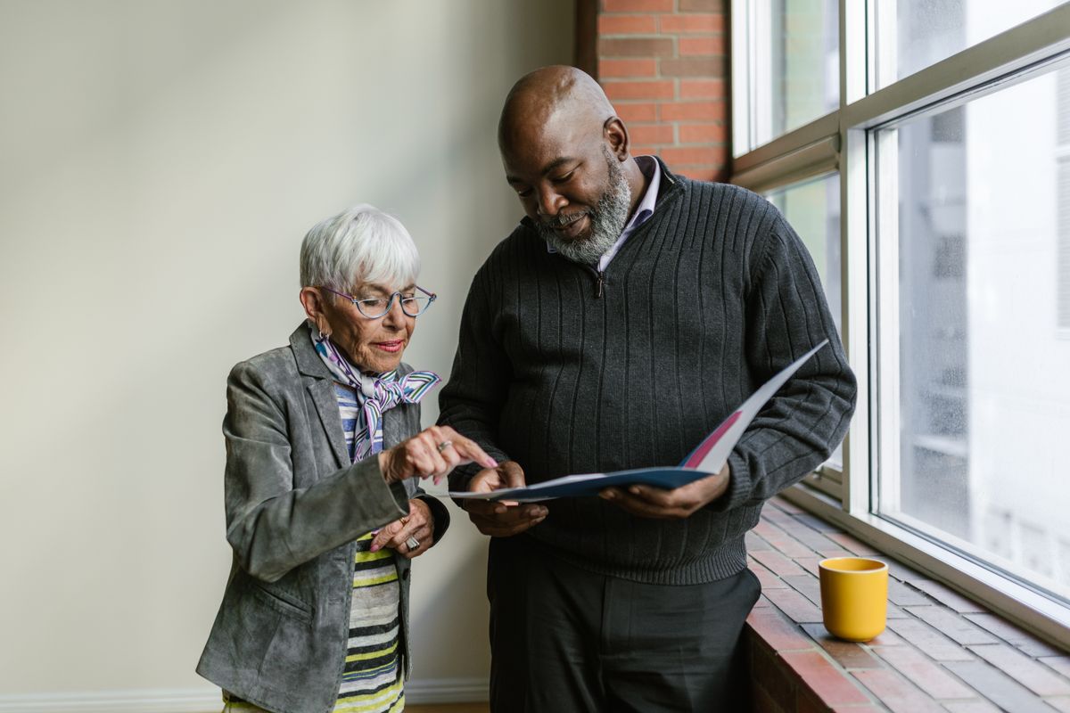 Two adults reviewing an open folder beside a window; illustrative stock photograph.