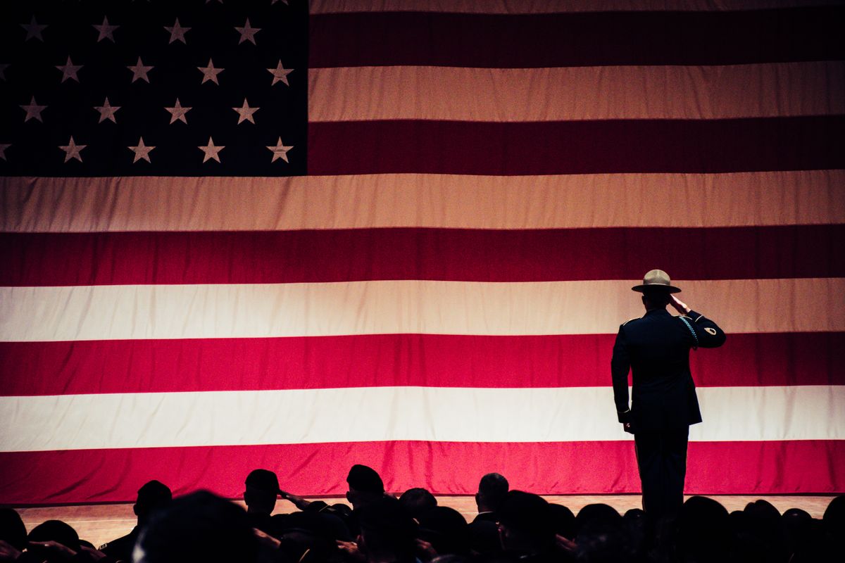 A service member saluting an American flag during a ceremony; editorial stock photograph.